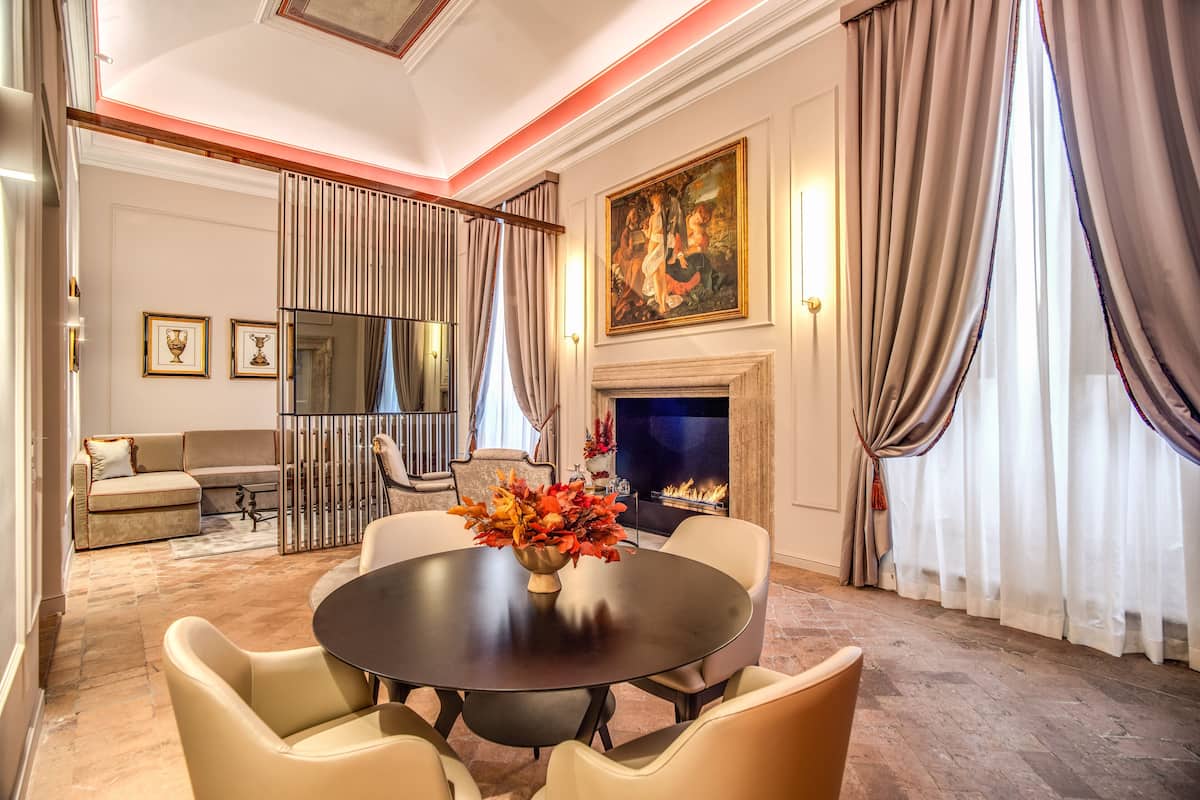 A formal dining room with a round table, chairs, a vase of flowers, a fireplace, and a painting on the wall.