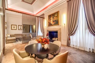 A formal dining room with a round table, chairs, a vase of flowers, a fireplace, and a painting on the wall.