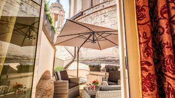 A sunlit outdoor seating area with wicker furniture, a large umbrella, and potted plants.