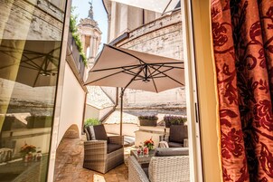A sunlit outdoor seating area with wicker furniture, a large umbrella, and potted plants.