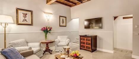 Una sala de estar con sofá, sillón, mesa de centro con fruta y televisor en la pared.