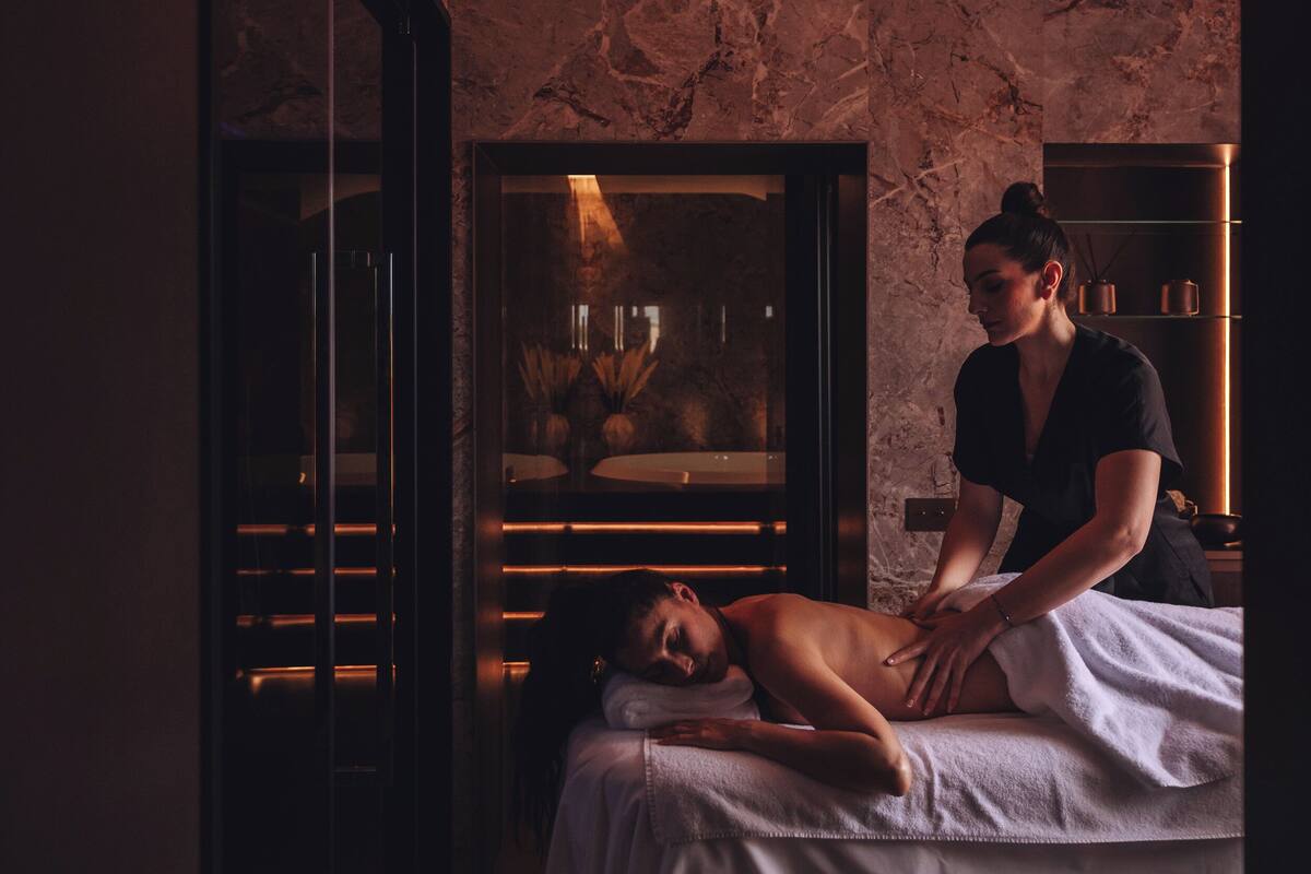 A spa room with a massage table, a person receiving a massage, and a massage table with a towel.