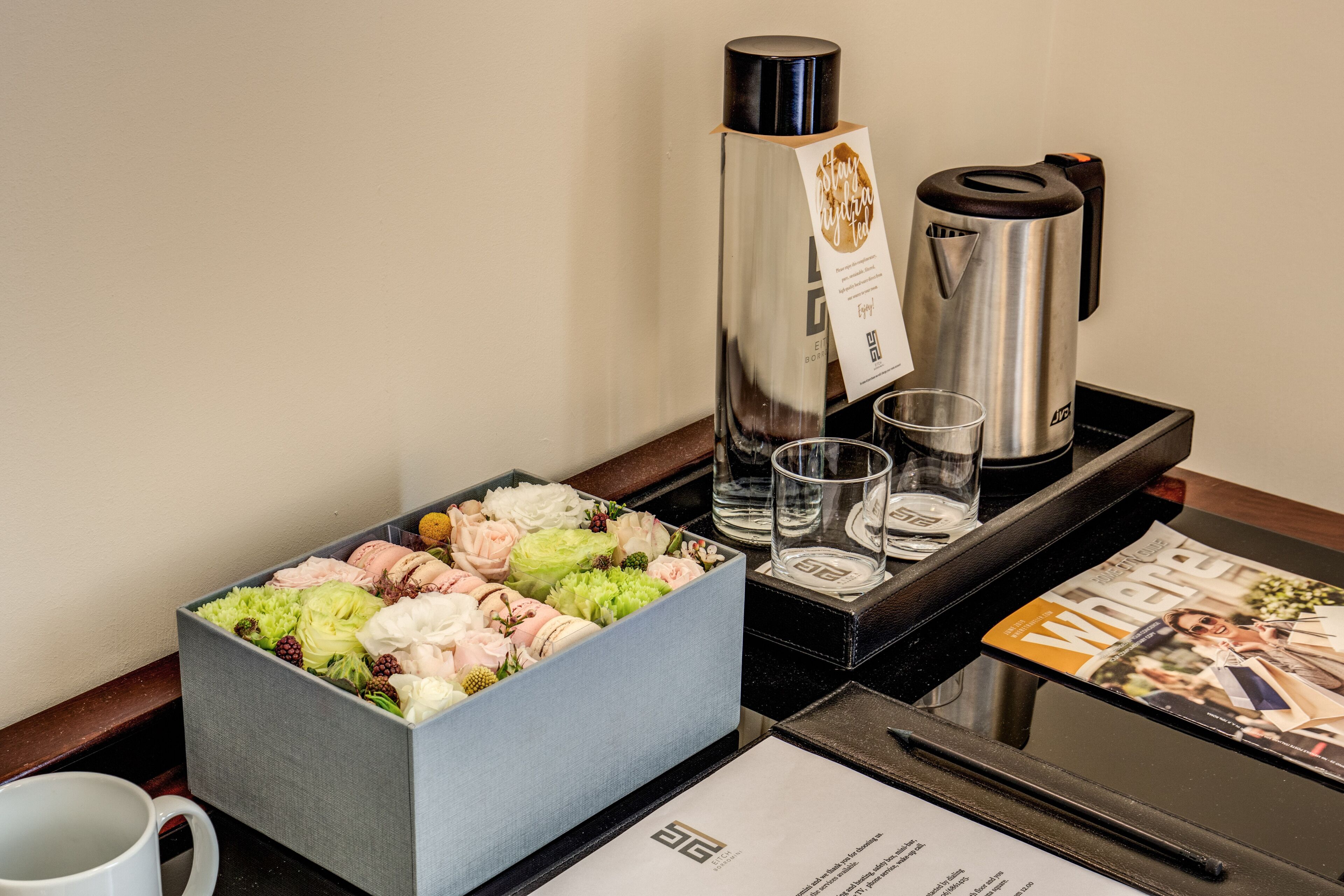 A hotel room's breakfast area with a box of assorted pastries, a coffee maker, glasses, and a menu.