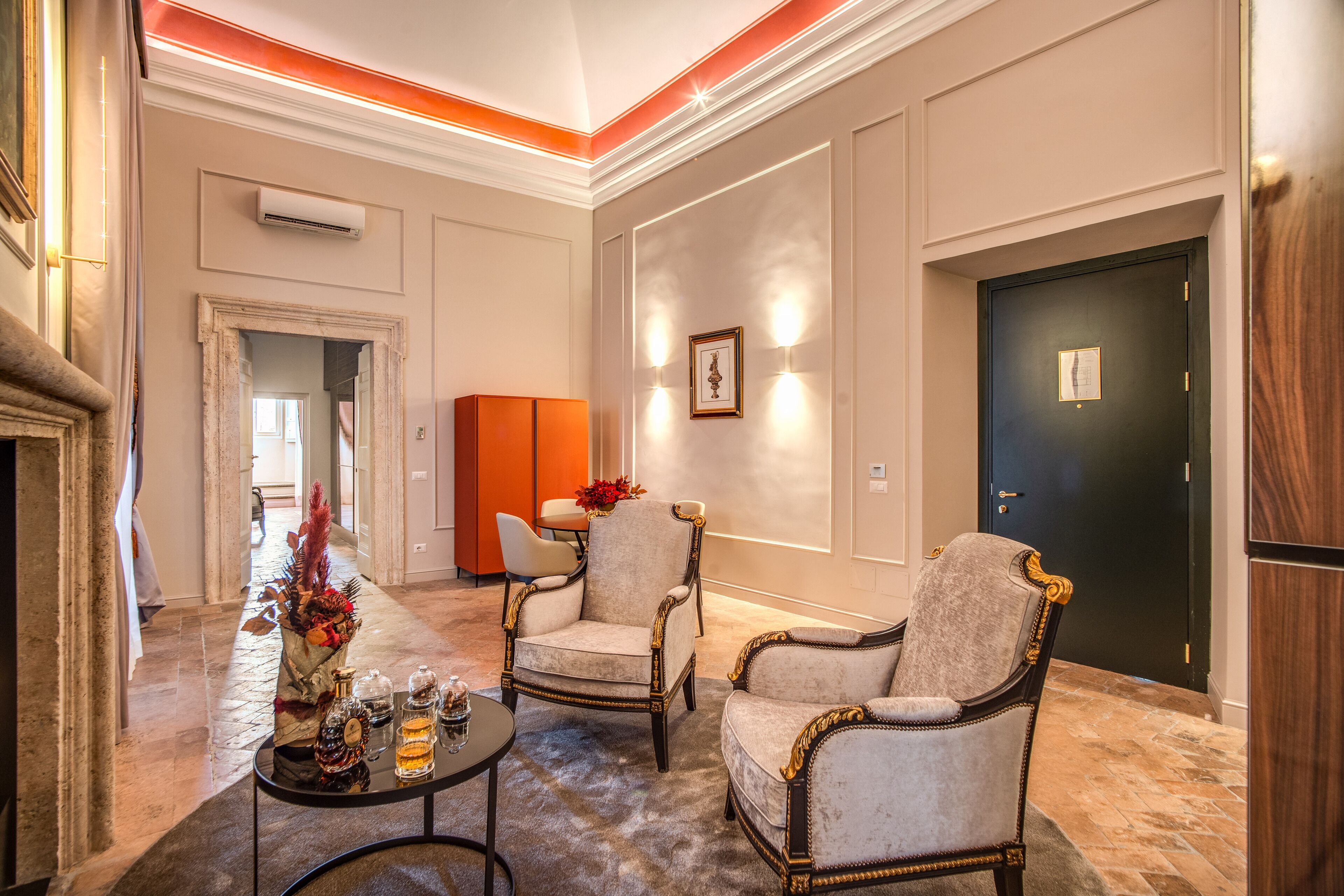 A spacious lobby with a fireplace, two armchairs, a coffee table with decorative items, and a door with a framed picture.