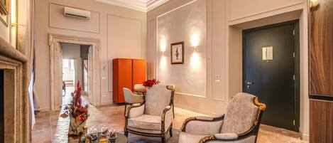 A spacious lobby with a fireplace, two armchairs, a coffee table with decorative items, and a door with a framed picture.