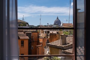 A view through a window of a cityscape with a prominent dome structure in the distance, surrounded by buildings with varied architectural styles and visible satellite dishes.