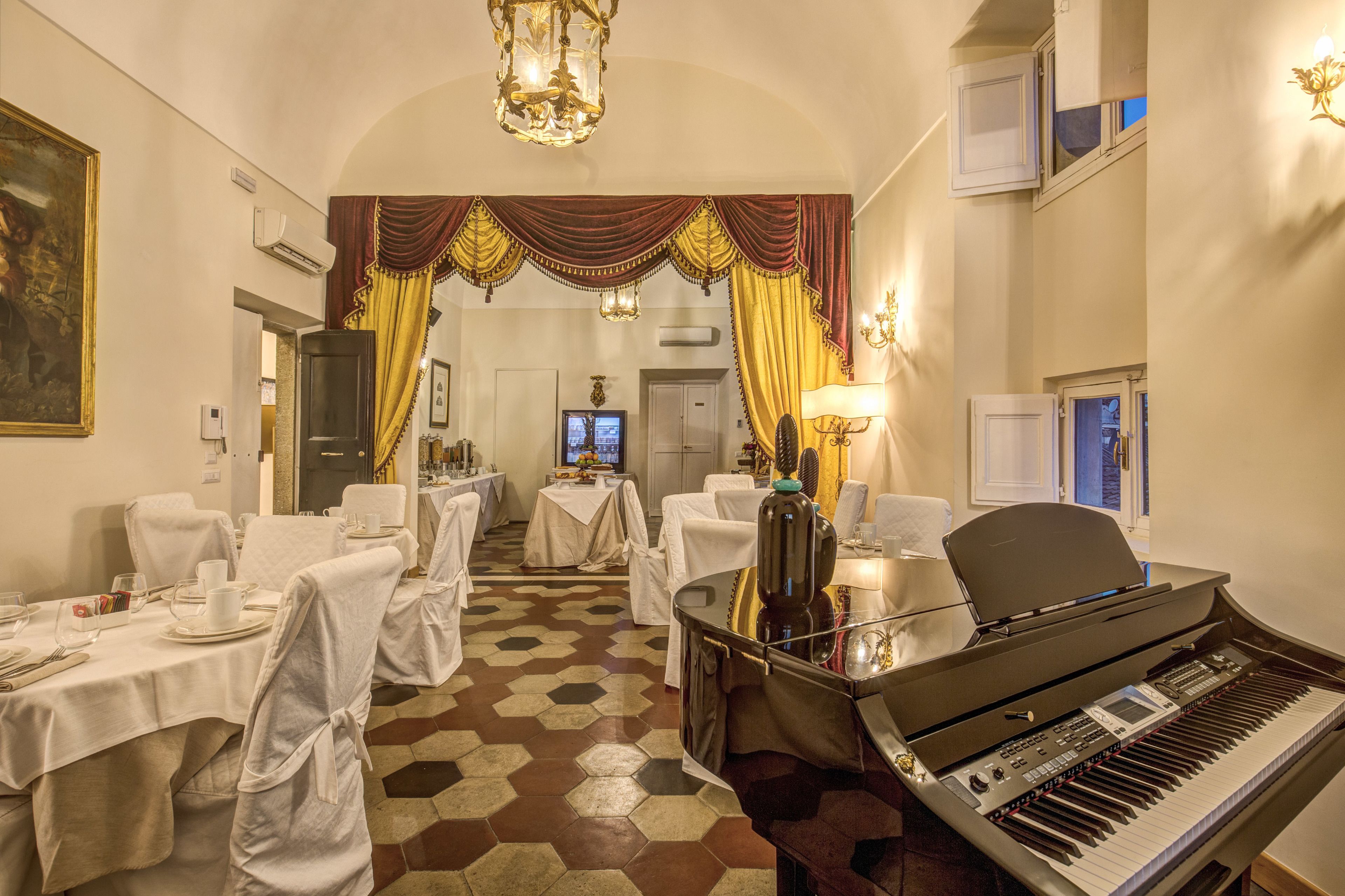 Una habitació d'hotel amb un piano, una zona de menjador amb taules preparades per a un àpat i un quadre gran a la paret.