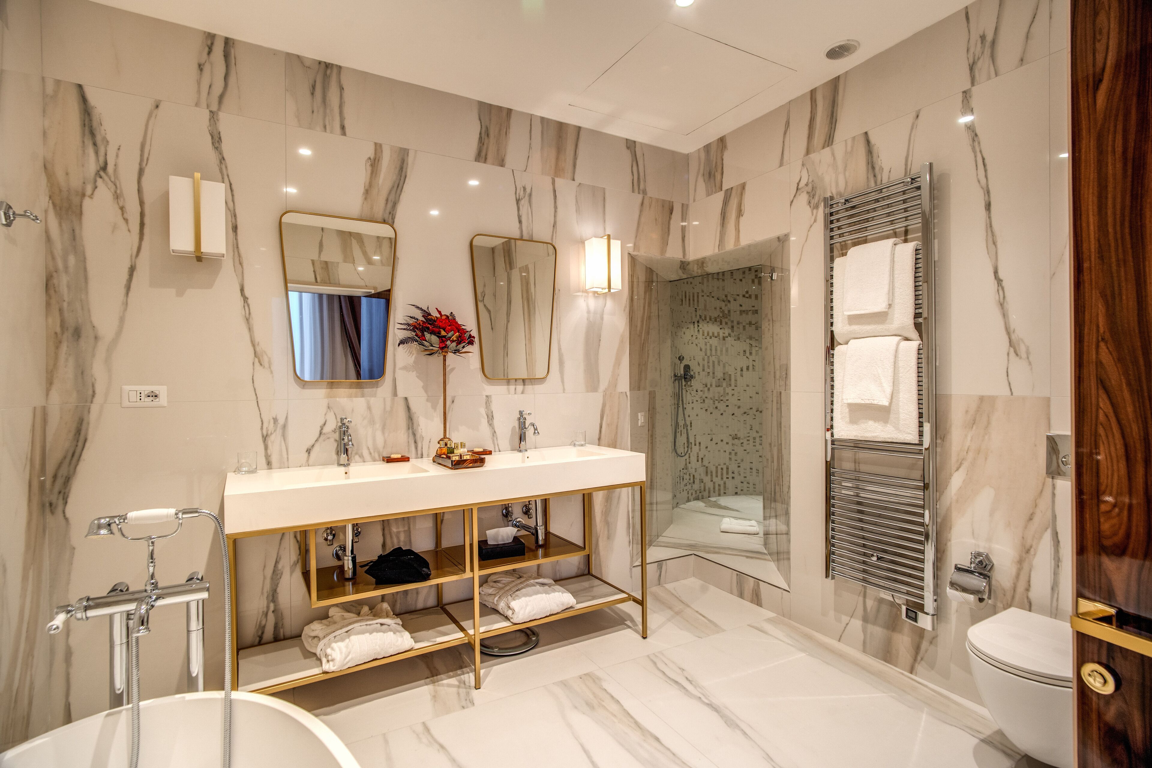 A modern bathroom with a marble vanity, a freestanding bathtub, a glass-enclosed shower, and a wooden door.