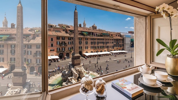 A window view of a historic square with buildings, a fountain, and a statue.