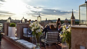 A rooftop terrace with seating and tables, overlooking a cityscape with historical buildings.