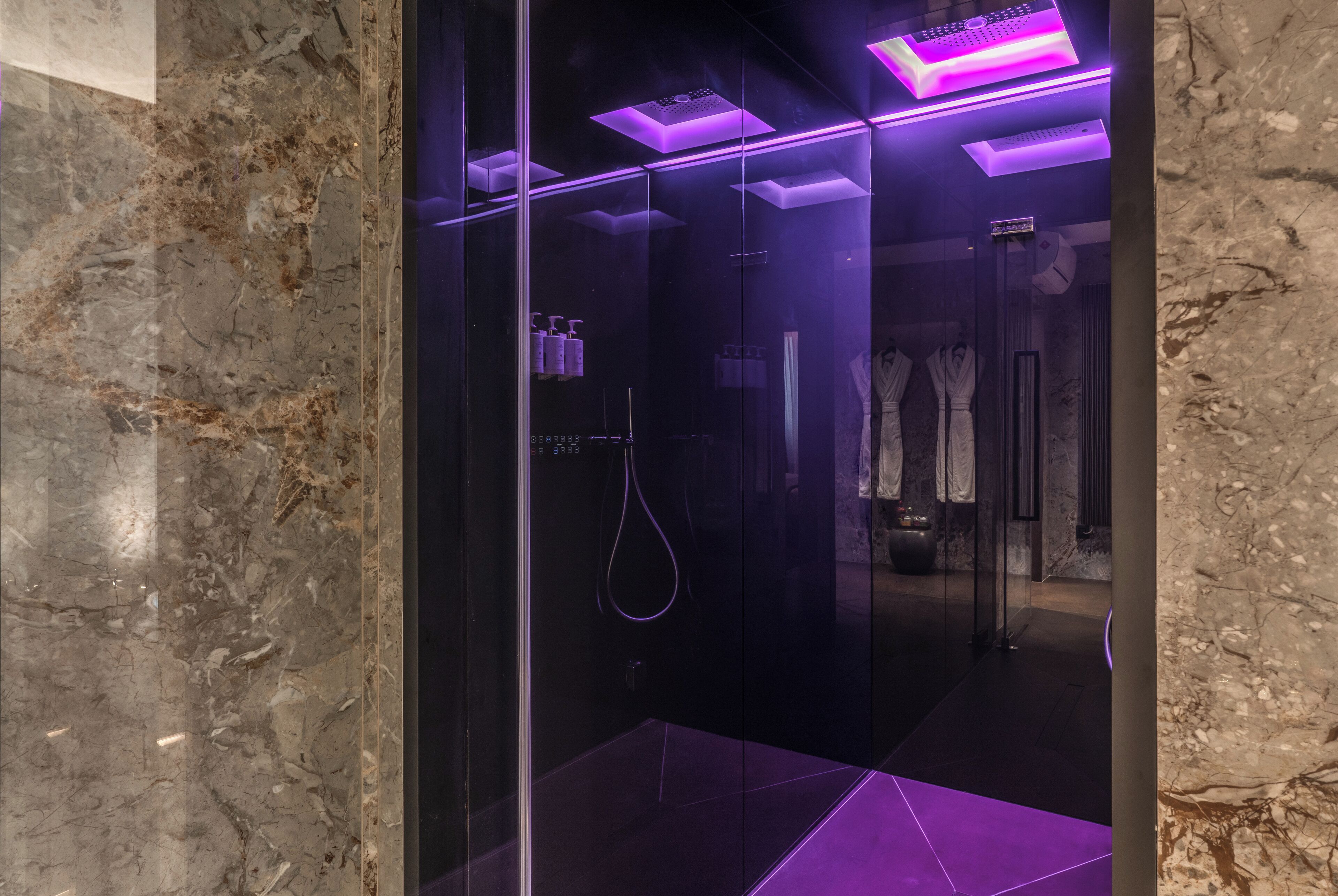 Ein modernes Badezimmer mit Glasabtrennung, Marmorboden und violetter Beleuchtung.