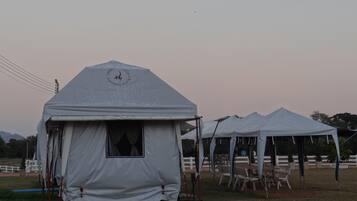 A series of white tents with a logo on the front, set up in an open field with chairs and tables arranged outside.