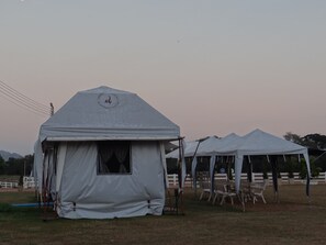 A series of white tents with a logo on the front, set up in an open field with chairs and tables arranged outside. - The Camping Field (Suan Phueng)