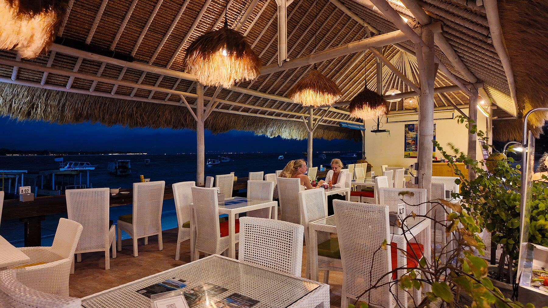 An outdoor dining area with wicker furniture and a view of the sea at night.
