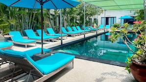 Un espace aménagé au bord de la piscine, avec des chaises longues et des parasols, entouré de verdure.