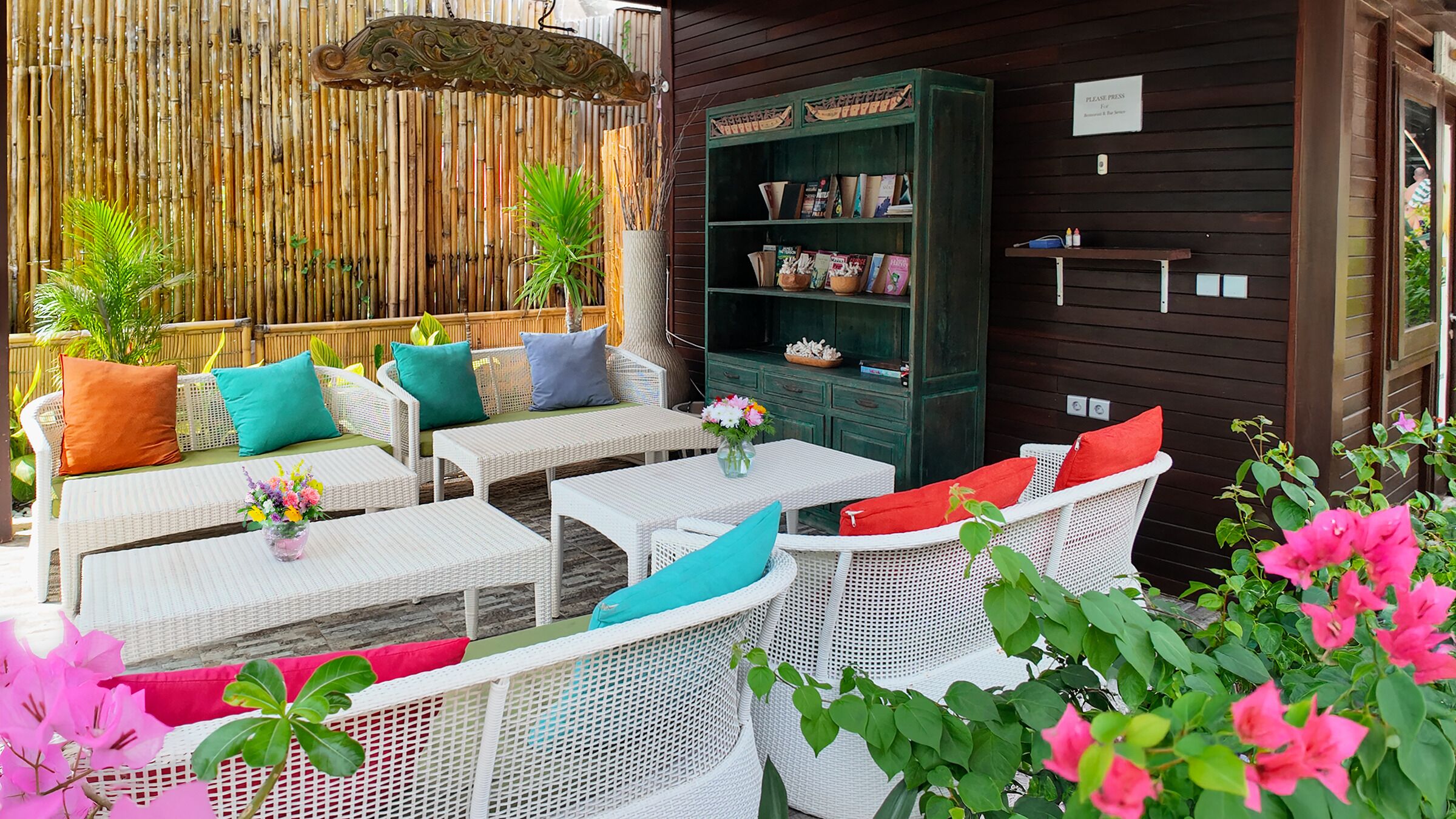 An outdoor seating area with wicker furniture, cushions, and a green bookshelf.