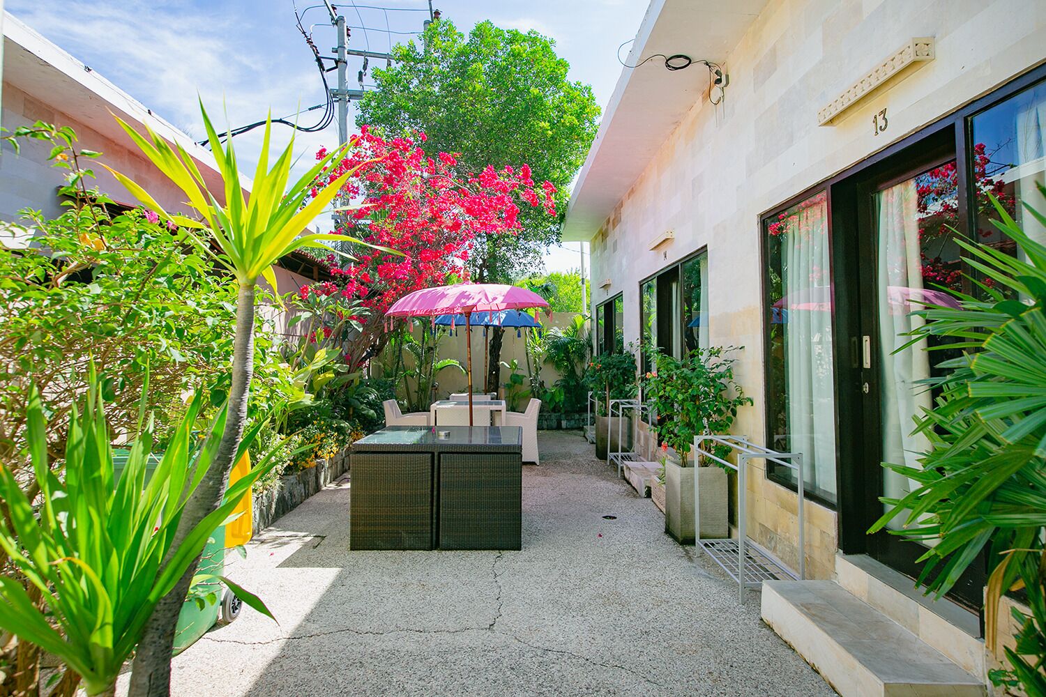 Une cour avec un espace aménagé pour s’asseoir, des plantes en pot et un bâtiment portant le numéro « 13 ».