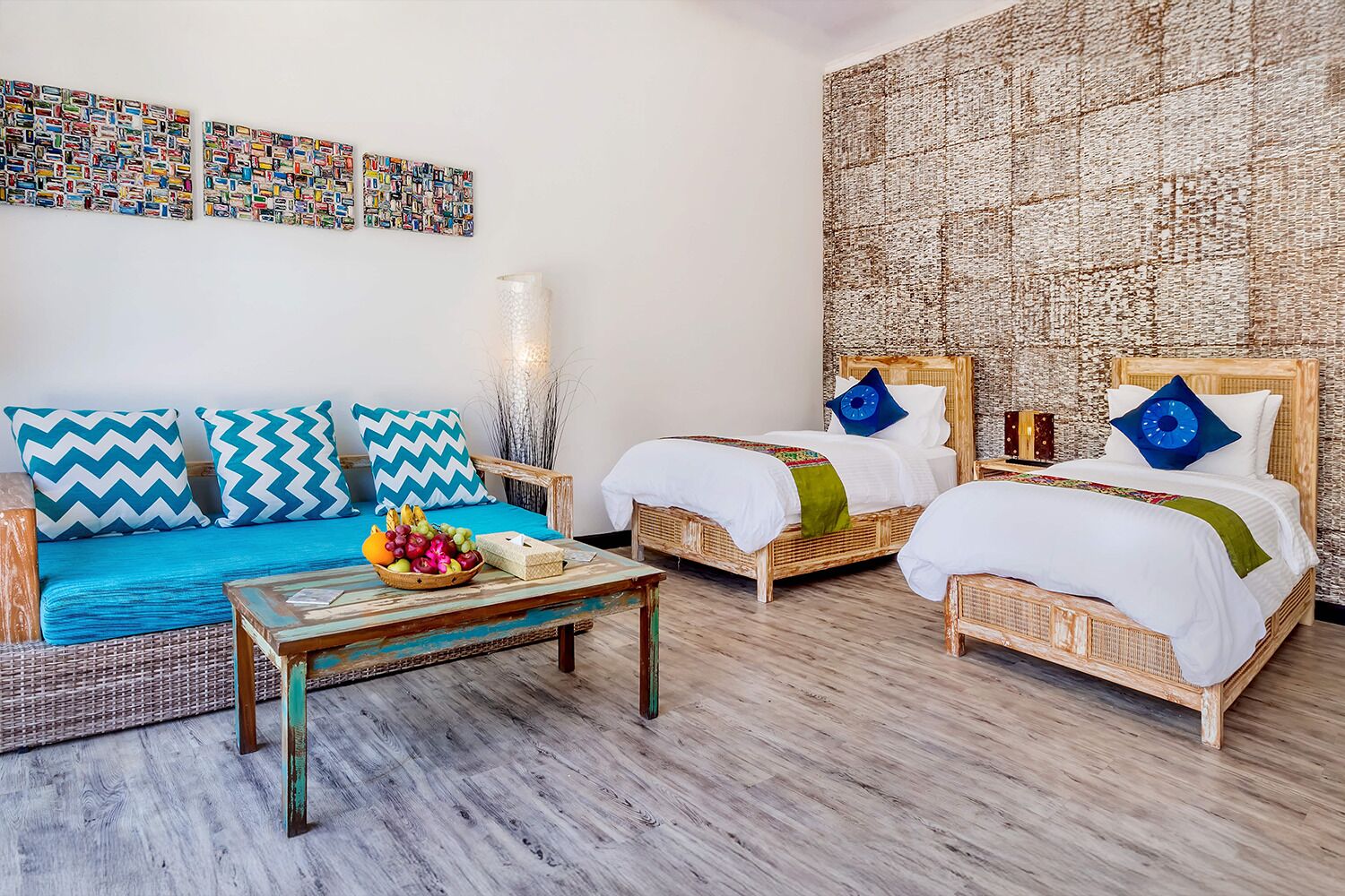 A room with two wicker beds, a blue sofa, and a wooden coffee table with fruit.
