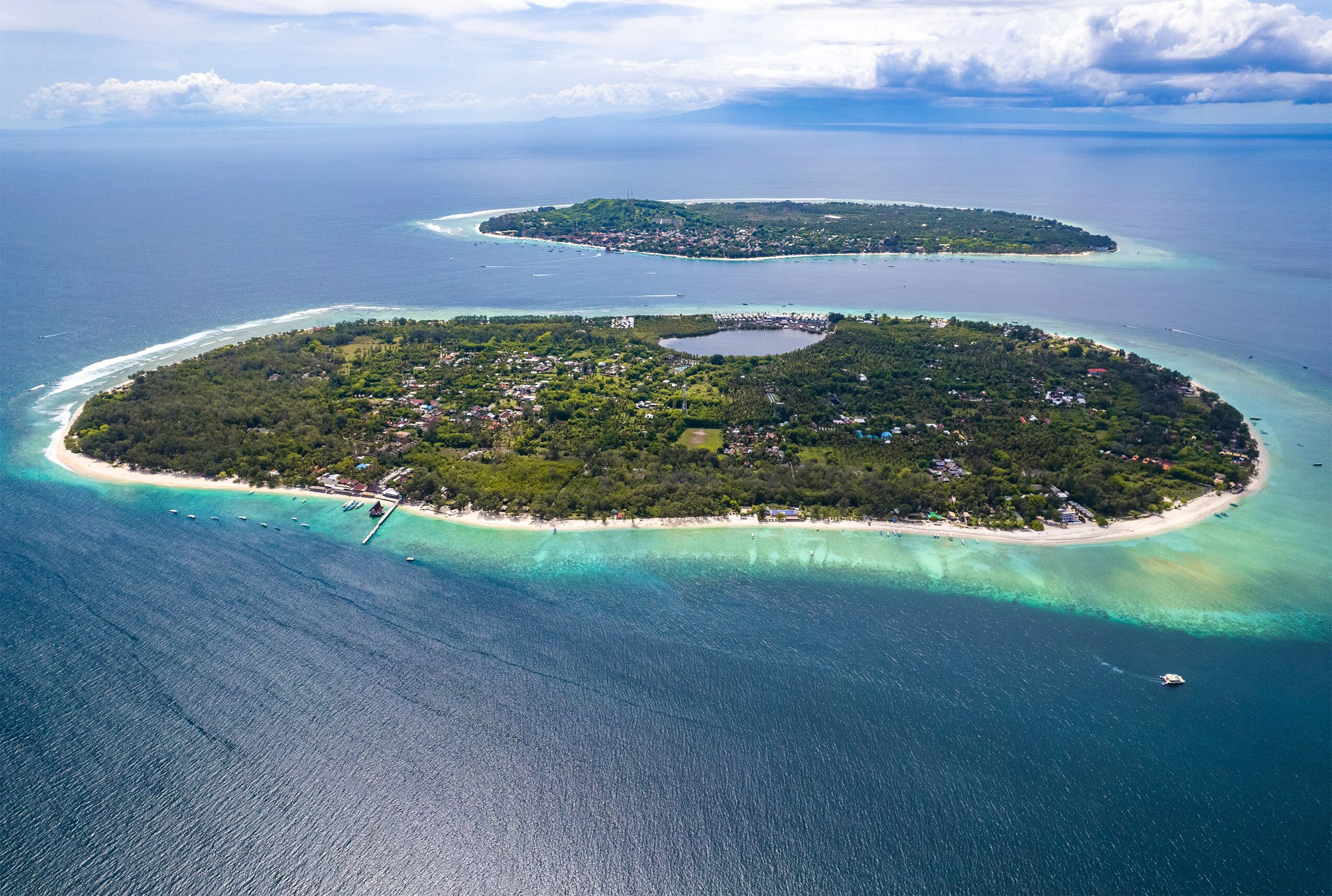 An aerial view of a tropical island with clear turquoise waters, a central lagoon, and a small settlement with buildings and vegetation.