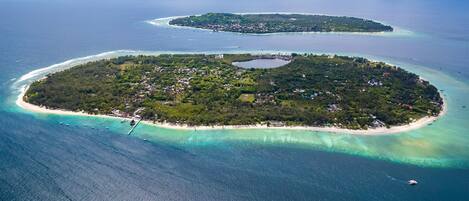 An aerial view of a tropical island with clear turquoise waters, a central lagoon, and a small settlement with buildings and vegetation.
