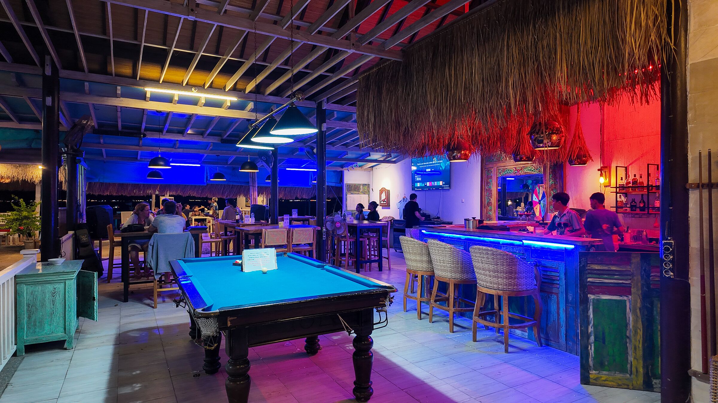 A pool table in a bar area with a thatched ceiling and wooden beams.