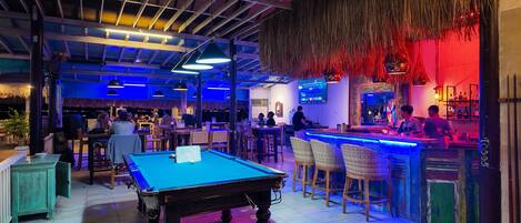 A pool table in a bar area with a thatched ceiling and wooden beams.