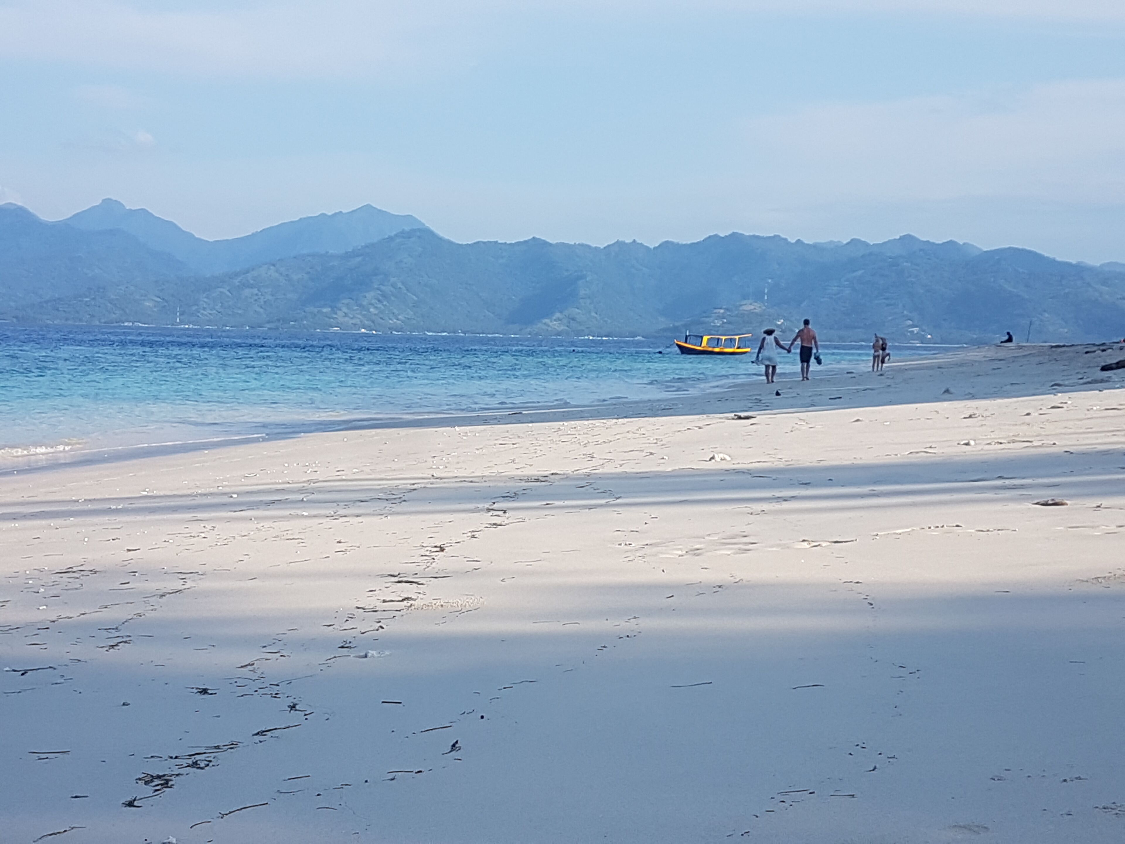 Una playa con un bote, montañas al fondo y huellas en la arena.