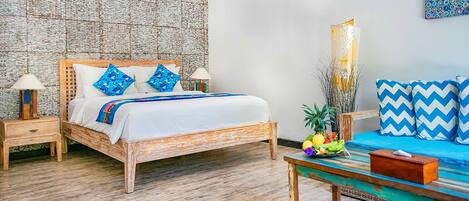 A bedroom with a wooden bed, two bedside tables, a nightstand, a bedside lamp, a small table with a bowl of fruit, and a colorful wall hanging.
