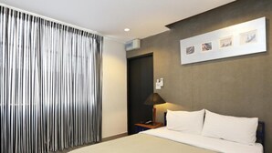 Quarto de hotel com cama, mesa de cabeceira, luminária, ar-condicionado fixado na parede e janela com persianas verticais.