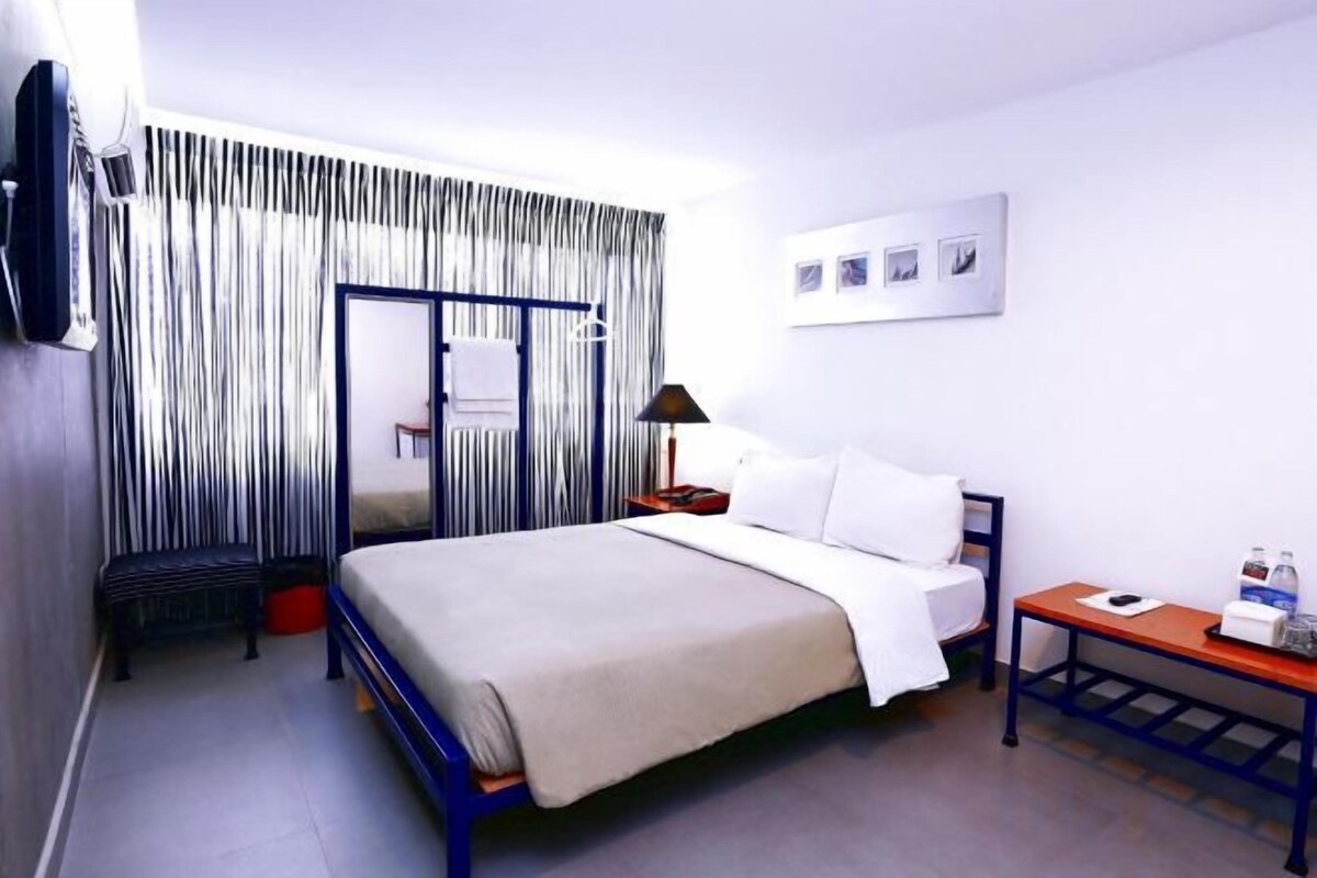 A hotel room with a bed, bedside table, lamp, and a mirror.