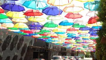 A street lined with parked cars and colorful umbrellas hanging overhead.