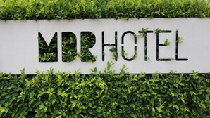 Placa para MDRHOTEL com fundo branco e folhagem verde integrada nas letras.