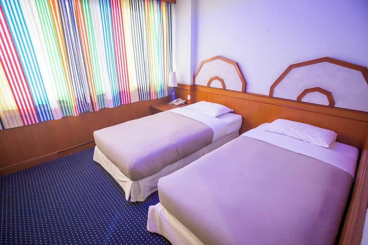 A hotel room with two single beds, a wooden headboard, a telephone, and a window with colorful curtains.
