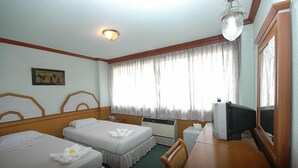 A hotel room with two beds, a desk, a television, and a window with curtains.