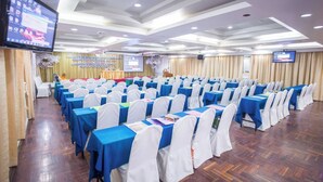 A conference room with rows of tables, white chairs, and a stage with a podium.
