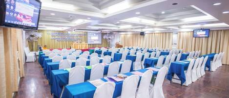 A conference room with rows of tables, white chairs, and a stage with a podium.