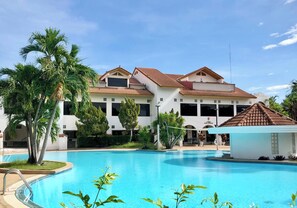 A resort with a large swimming pool, palm trees, and a two-story building with a tiled roof. - DadD Resort by Lopburi Inn Resort (Lop Buri)