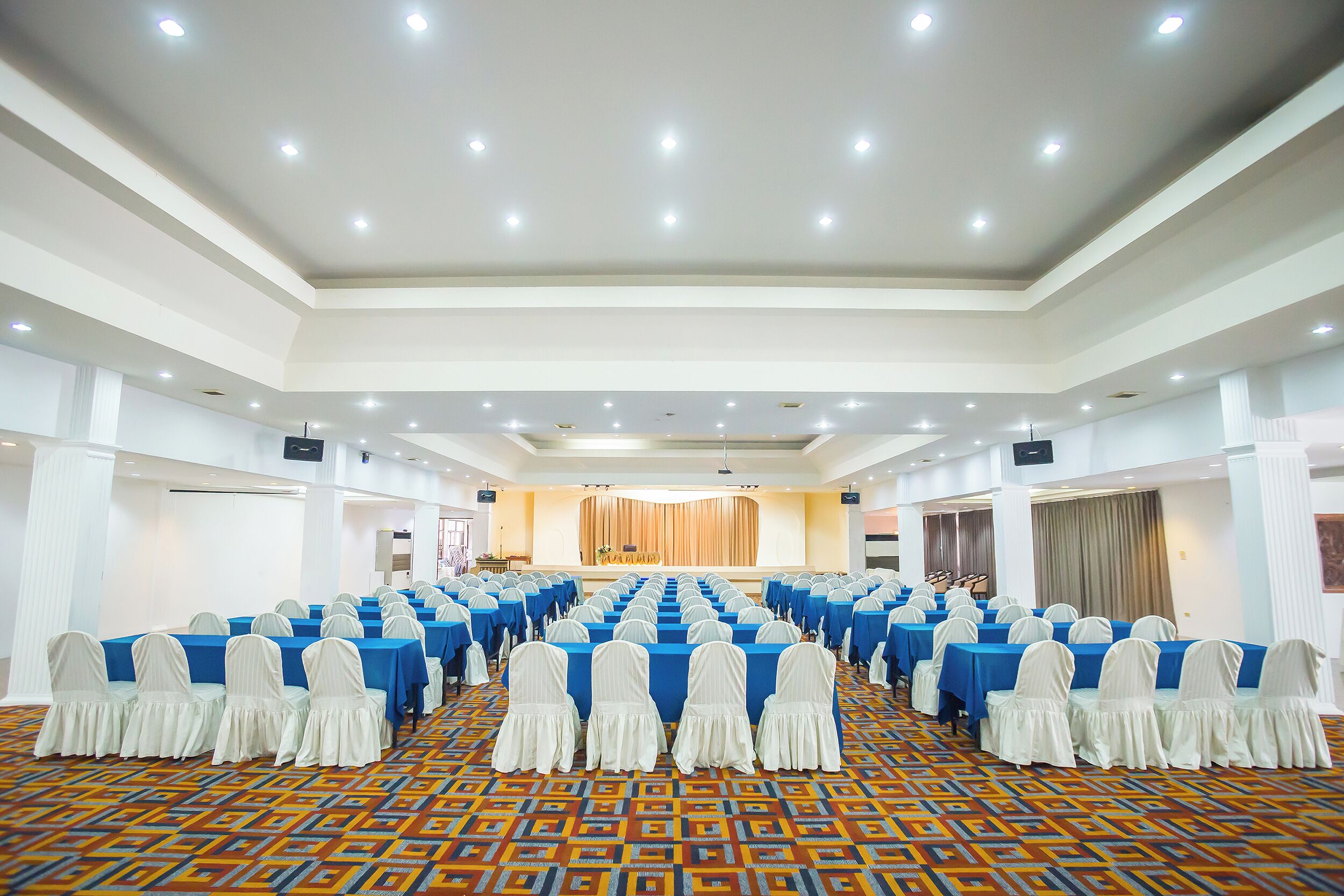 A large conference room with rows of tables, white chairs, and a stage at the front.
