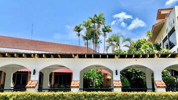 A building with a tiled roof, arched walkways, and a row of palm trees.