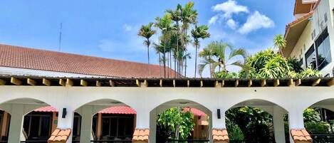 A building with a tiled roof, arched walkways, and a row of palm trees.