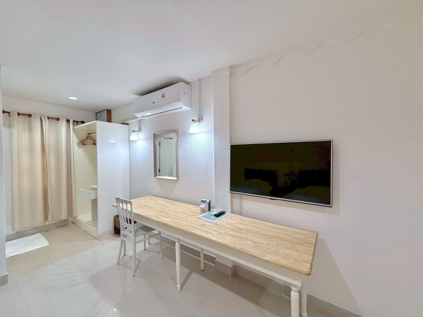 A modern hotel room with a wooden desk, a chair, a mirror, a television, and a wardrobe.