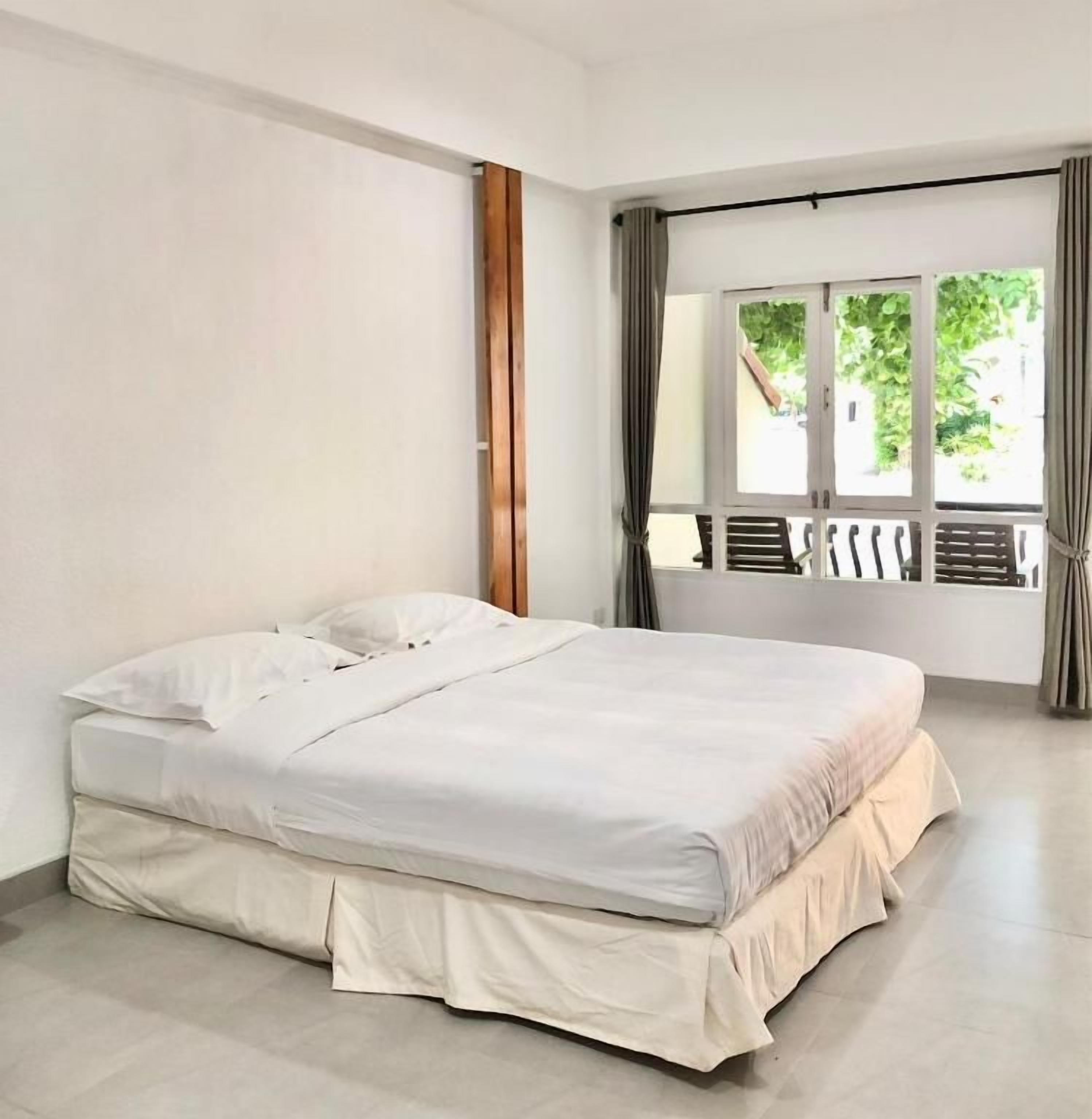 A single bed in a room with a large window and curtains.