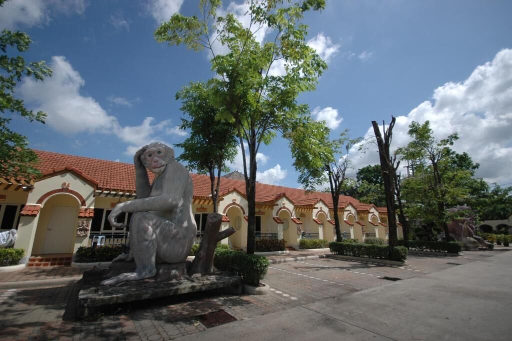 A statue of a seated figure in a courtyard with a building featuring arched doorways and a red-tiled roof.