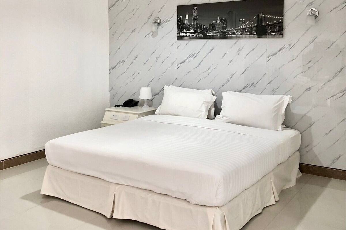 Moderni hotellihuone, jossa on suuri sänky, yöpöytä, lamppu ja kaupunkimaisemaa esittävä taulu seinällä.