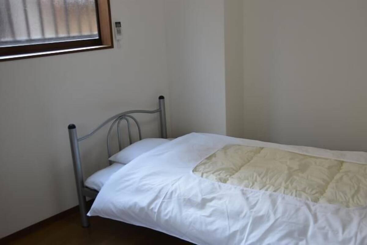 A single bed with a metal frame, white bedding, and a quilt.