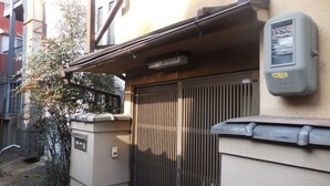 Una entrada protegida con un portón metálico, un cuadro de electricidad en la pared y una pequeña estructura con puerta.