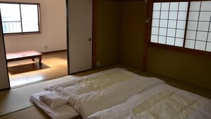 Una habitación japonesa tradicional con suelo de tatami, un futón, puertas correderas y vistas a un balcón.