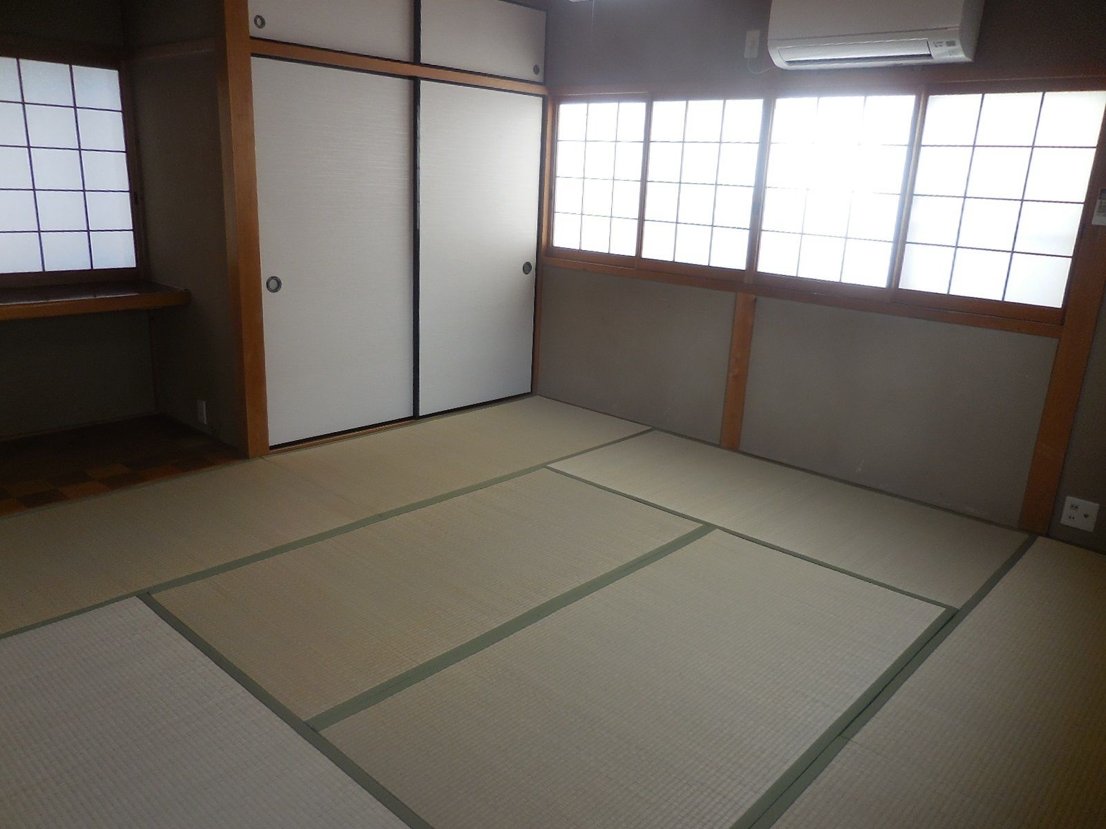 A traditional Japanese room with tatami flooring, sliding doors, and a window with a grid pattern.