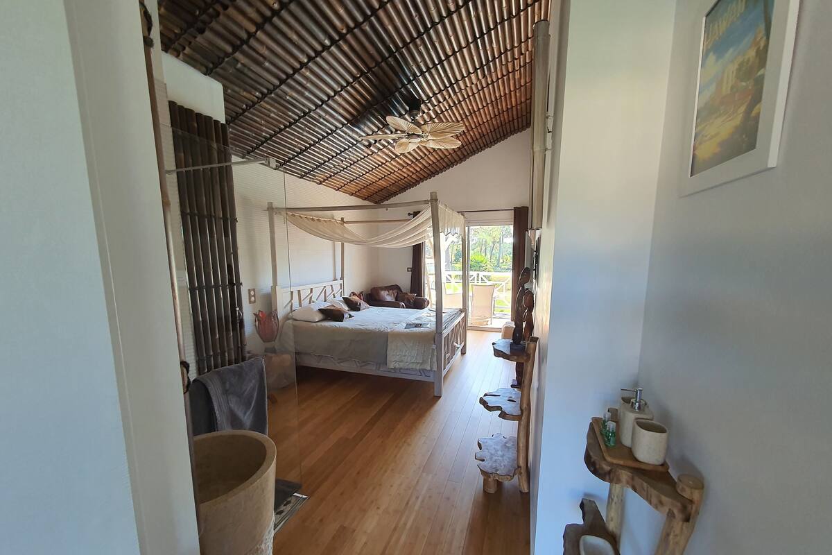 A bedroom with a canopy bed, wooden flooring, and a view of the outdoors.
