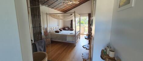 A bedroom with a canopy bed, wooden flooring, and a view of the outdoors.